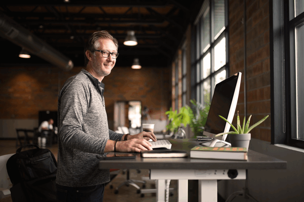Homme souriant travaillant debout devant un ordinateur dans un espace de coworking lumineux