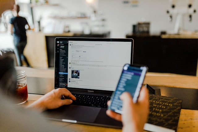Vue rapprochée d’un utilisateur consultant Slack sur un ordinateur portable tout en tenant un smartphone