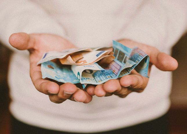 Mains tendues tenant plusieurs billets en euros